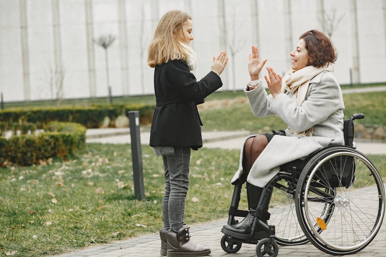 Happy child and woman in wheelchair sharing a joyful moment outdoors.